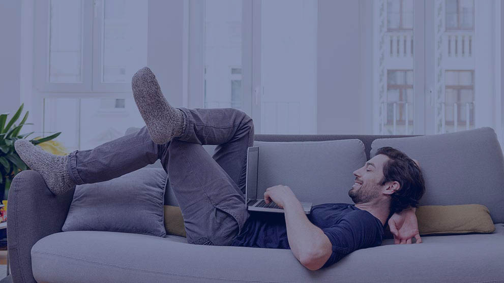 Relaxed man lying on couch using laptop